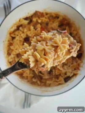 A serving spoon scooping up a hearty portion of chili mac and cheese from a rustic pot.