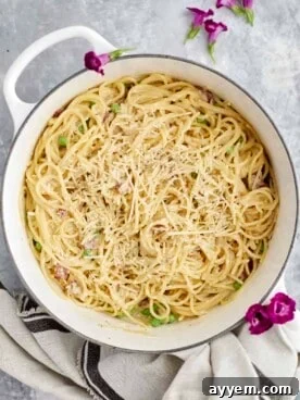 Overhead view of creamy one-pot spaghetti carbonara in a white pot, garnished with black pepper.