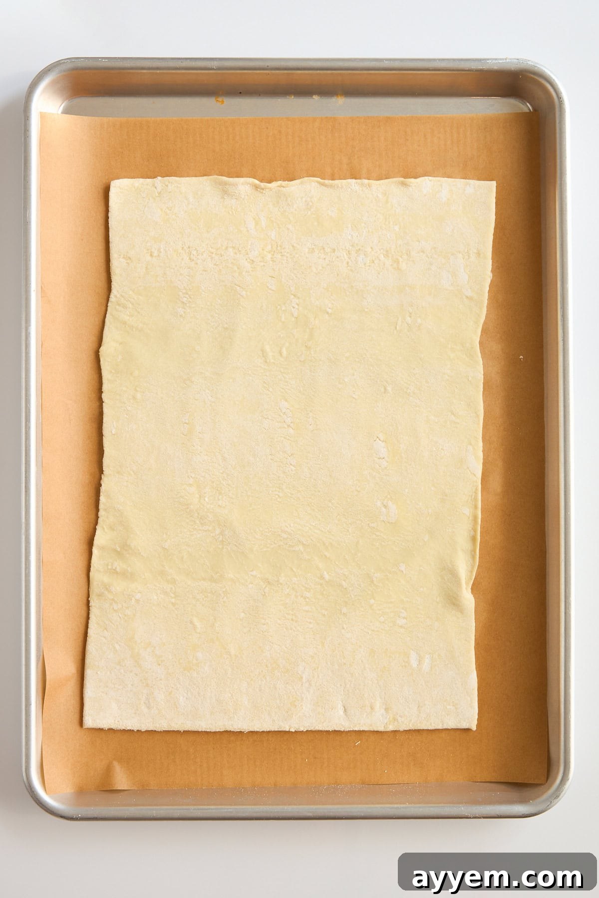 A sheet of uncooked puff pastry is placed on a piece of parchment paper on a baking tray, ready for baking.