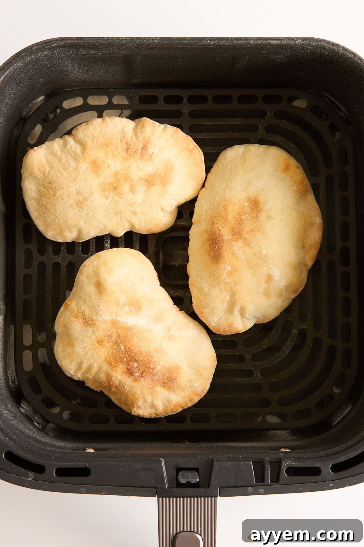 Three pieces of golden-brown flatbread are placed inside the basket of an air fryer, viewed from above on a white background.
