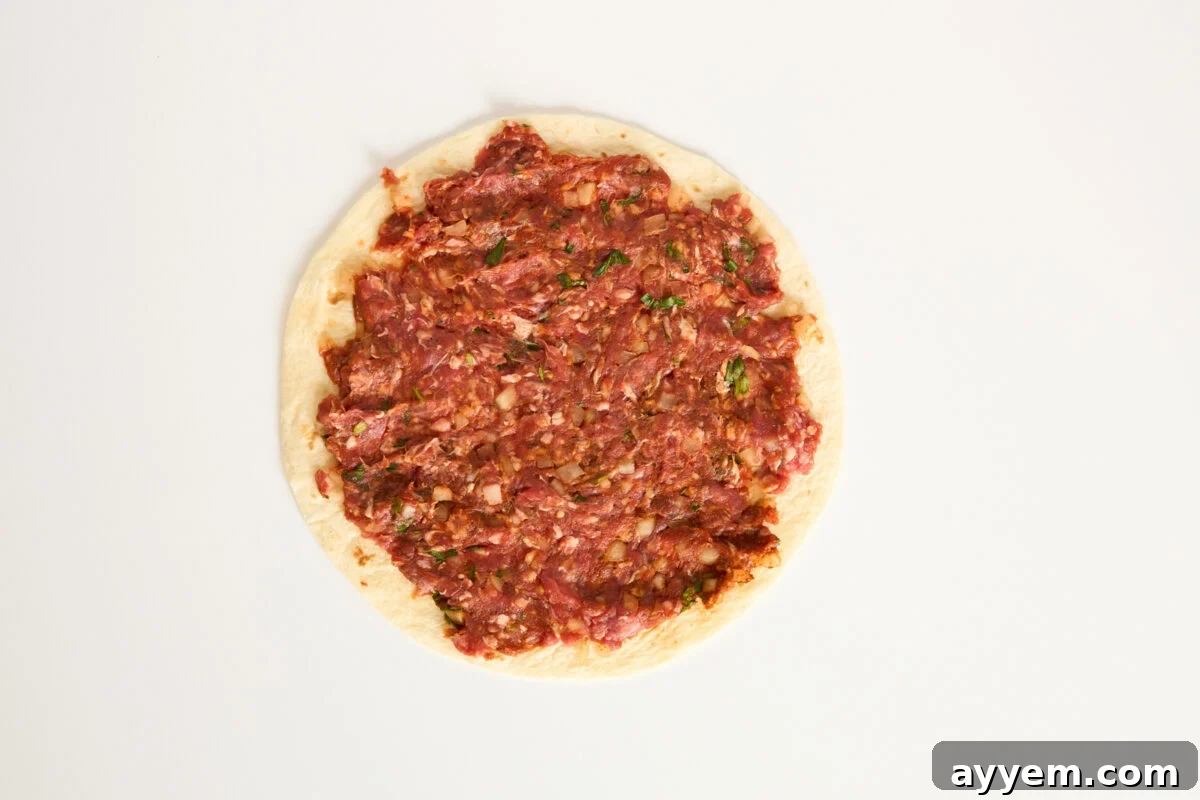 A round piece of flatbread topped with a raw, finely minced meat mixture, spread evenly to the edges, on a plain white background.