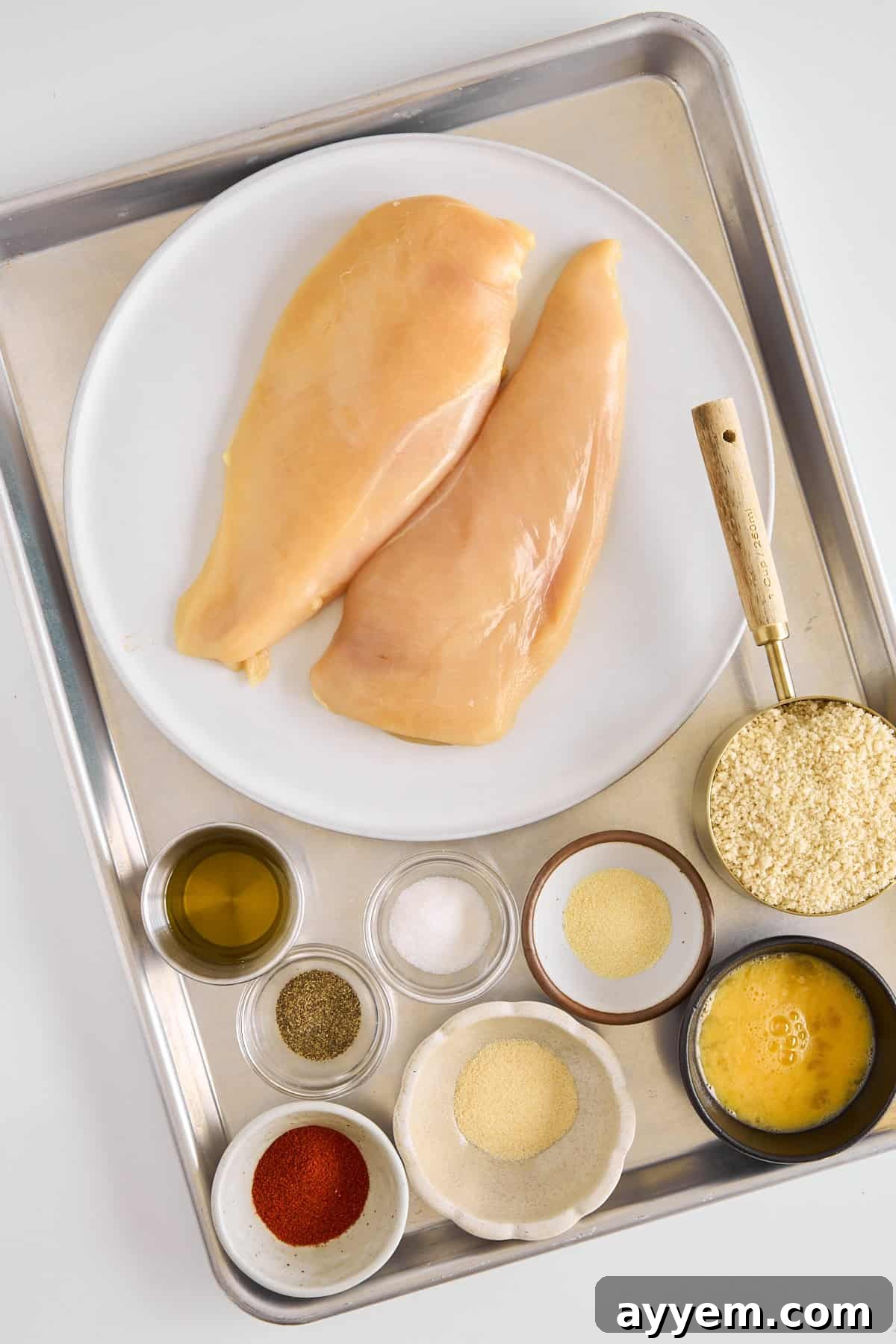 A plate of raw chicken breasts and various spices.