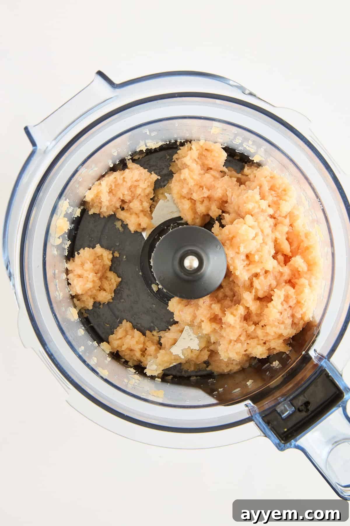 A top-down view of a food processor containing ground chicken and onions, partially blended, on a white background.