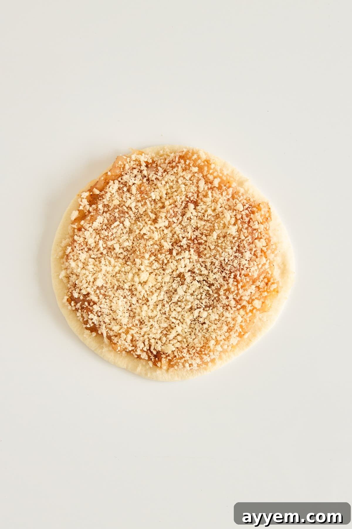 A round piece of dough topped with a crumbly brown sugar and cinnamon mixture, placed on a plain white background.
