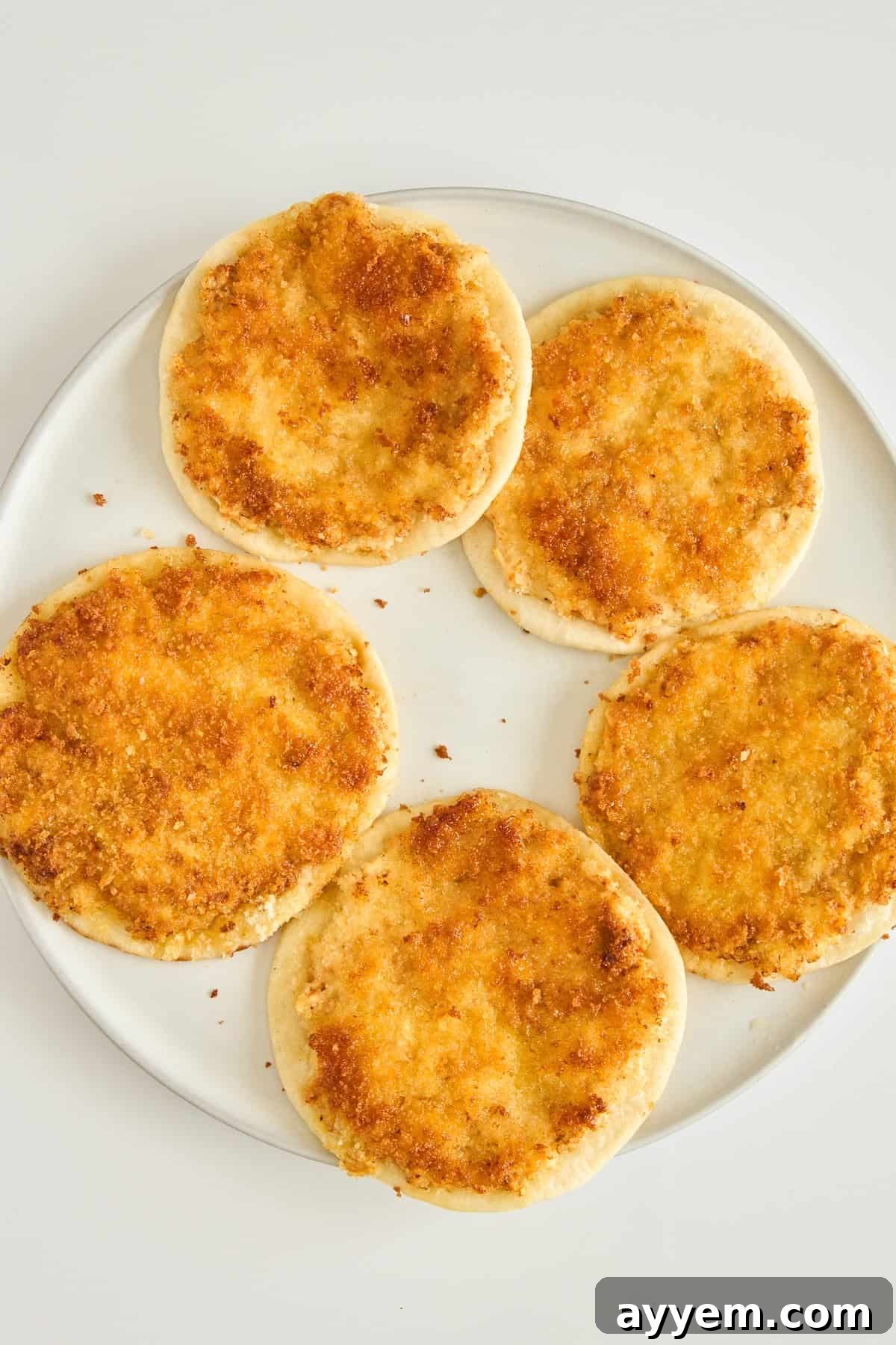 A plate with five round flatbreads topped with a golden, crispy layer, arranged in a circular pattern on a white background.