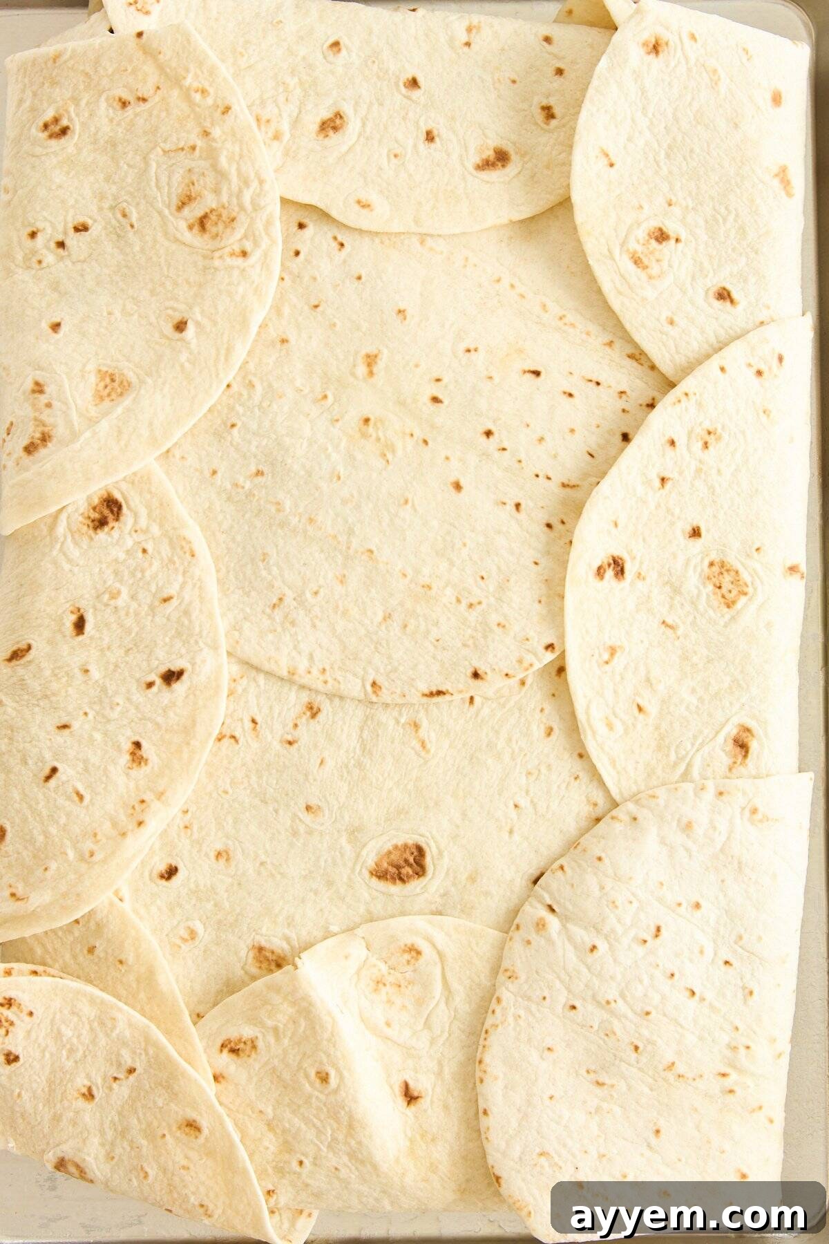 A rectangular baking dish lined with overlapping flour tortillas, covering the bottom and sides, creating a sturdy base for a sheet pan bake.