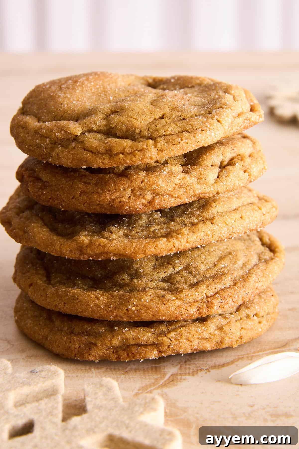 Why Are My Cookies So Flat 4 A stack of five golden brown cookies sits on a light wooden surface, with a white snowflake decoration nearby. The cookies appear soft and slightly chewy, with a sugar-coated texture.