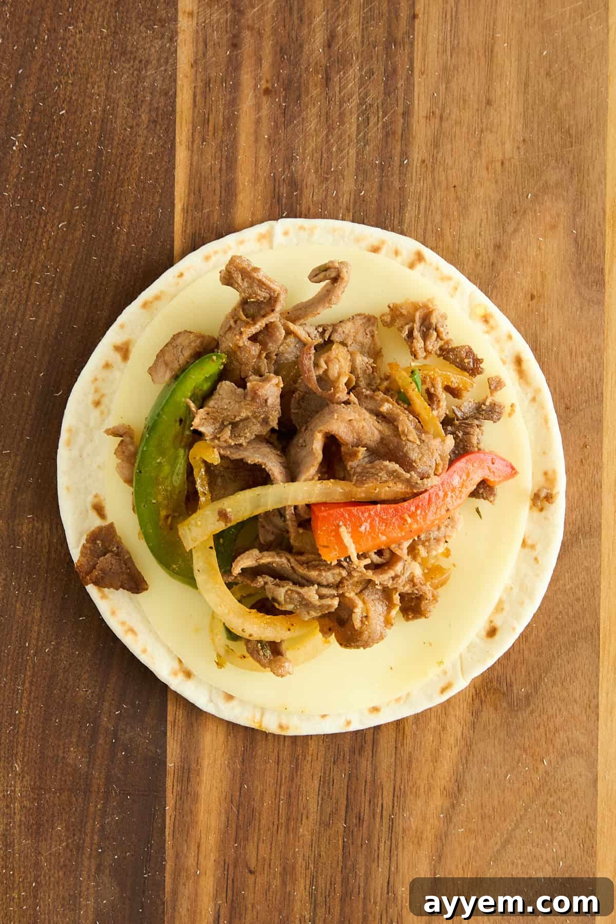 A warm tortilla generously filled with melted cheese, savory sliced beef, and vibrant green and red bell peppers, resting on a rustic wooden board.