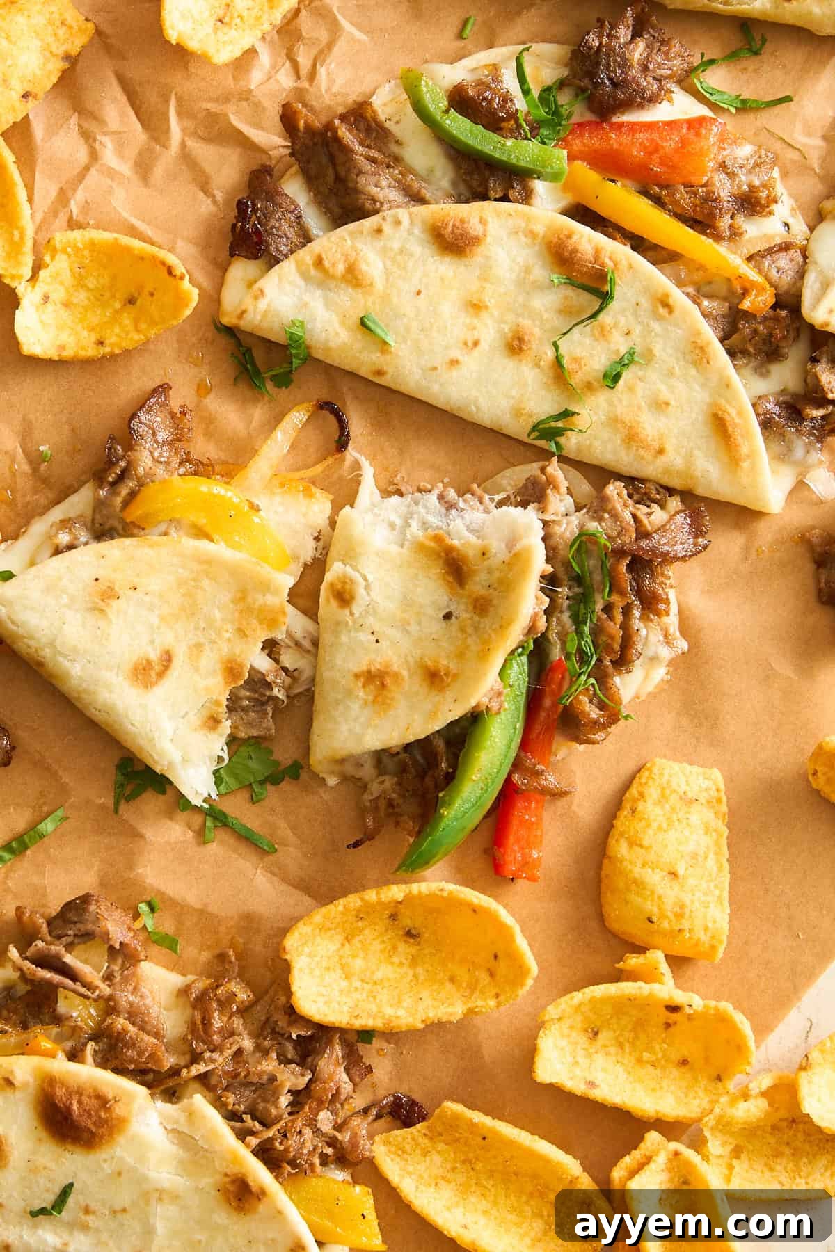 Soft tacos filled with shredded meat, yellow and green bell peppers, and herbs, served on brown parchment paper with crispy corn chips.