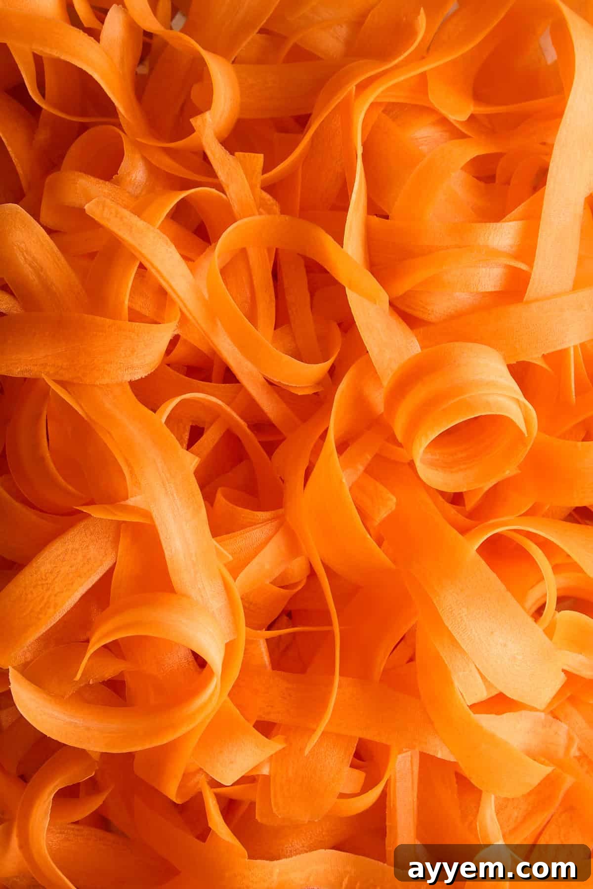 Thin, curly strips of bright orange carrot peel closely arranged in a random pattern, creating a textured and vibrant background.