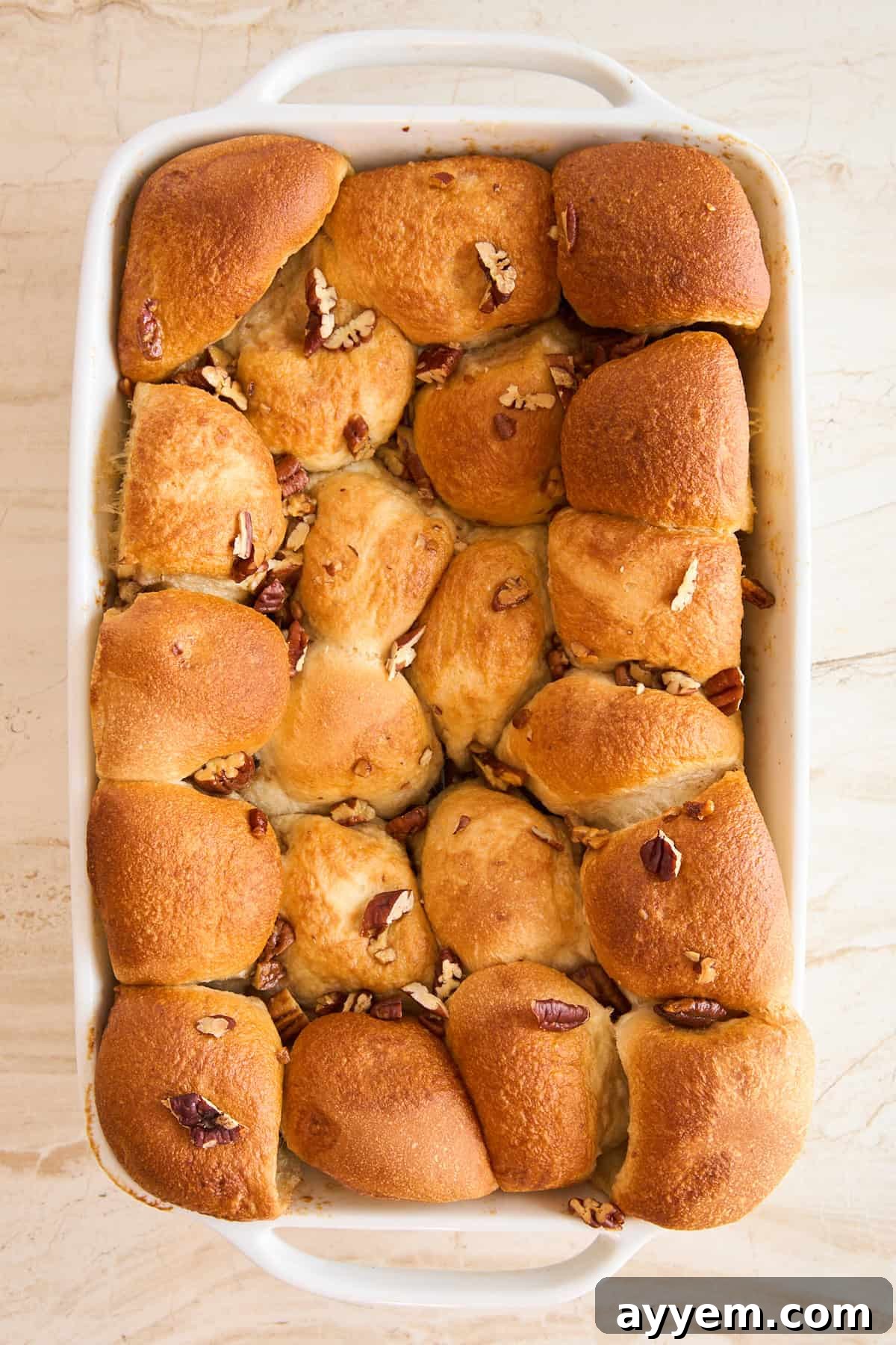 A white baking dish filled with golden-brown pull-apart rolls, beautifully risen and topped with chopped pecans, pre-bake.