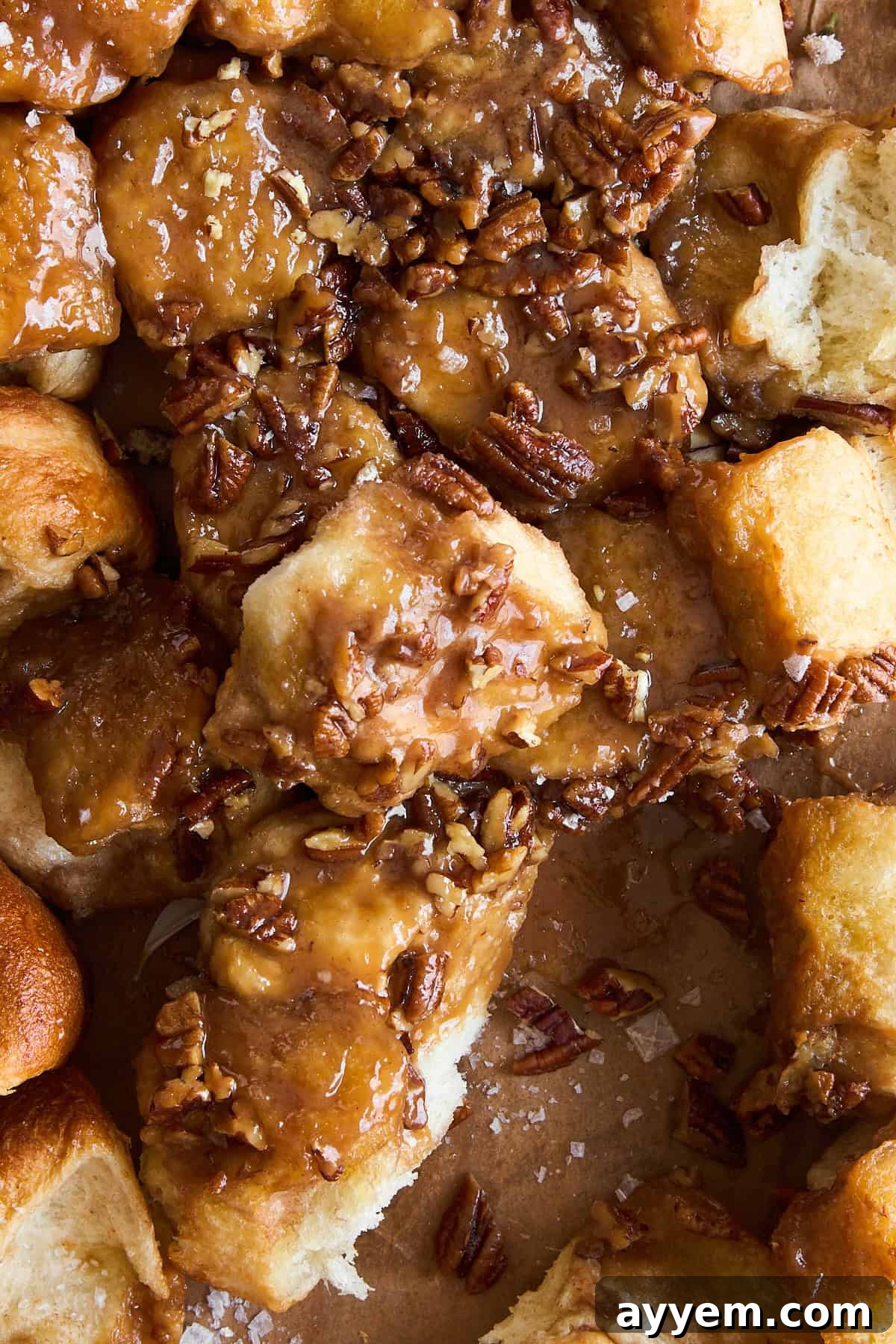 Close-up of golden brown sticky buns topped with caramel sauce and chopped pecans, with pieces pulled apart to reveal their soft, fluffy texture and gooey interior.