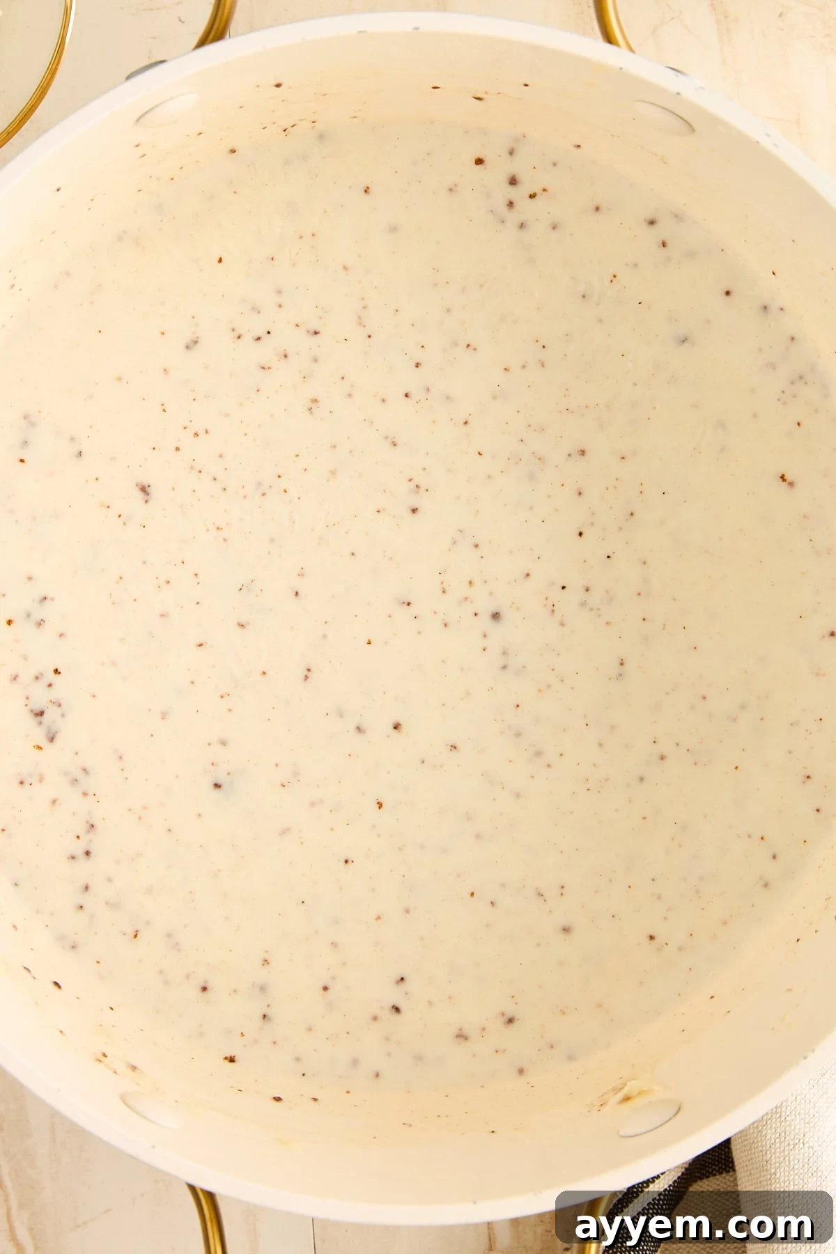 A chef pouring milk into a pot of roux, whisking to combine.
