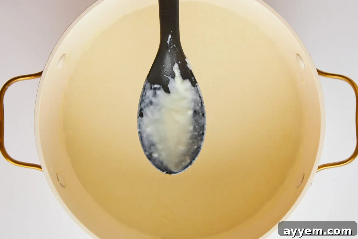 A close-up of a spoon stirring a perfectly smooth béchamel sauce.