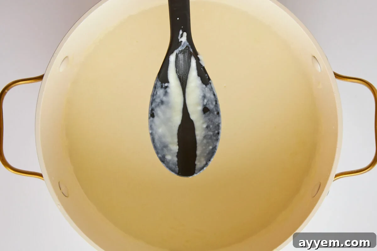 A spoon lifting a silky stream of béchamel sauce from a pot.